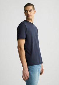 T-shirt blu navy a maniche corte con collo rotondo e un sottile dettaglio del logo, realizzato in tessuto morbido e liscio, abbinato a jeans azzurri.