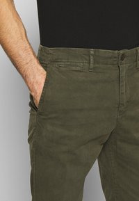 Olive green cotton pants featuring a straight cut, front and back pockets, and a button closure. Soft texture and casual style.