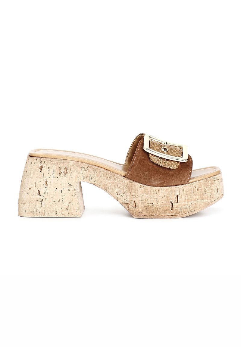 Mule en daim marron à bout ouvert avec une grande boucle dorée et un talon compensé épais en liège sur fond blanc.