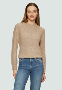 Beige gestrickter Pullover mit rundem Halsausschnitt, gerippter Textur und langen Ärmeln, kombiniert mit hellblauen Denim-Jeans.