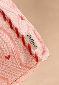 Różowy kosz do przechowywania z tkaniny o plecionej strukturze, zdobiony czerwonymi wzorami serc i kwiatów, z widoczną metką "Cath Kidston".