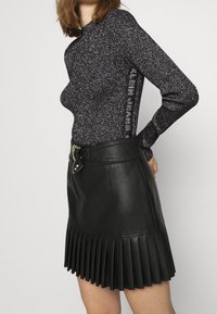 Czarny top z długim rękawem z metalicznymi nitkami, w połączeniu z czarną skórzaną plisowaną spódnicą z paskiem i srebrnymi detalami.