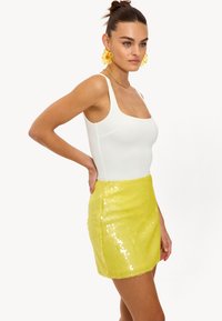 Gele pailletten mini-jurk met een rechte snit, gecombineerd met een aansluitende witte body. De stof heeft een glanzende, gestructureerde afwerking.