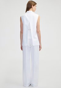 Witte mouwloze top met een rugsplit, gecombineerd met witte wijde broek. De stof lijkt lichtgewicht en soepel, met een strakke uitstraling.