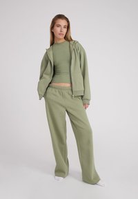 Haut à capuche vert avec zip, haut ajusté assorti et pantalon de survêtement ample. Texture lisse et douce avec un design décontracté et une taille élastique.