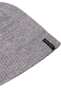 Grijze gebreide beanie met een geribbelde textuur en een zwart etiket met witte tekst. Het ontwerp is eenvoudig en aansluitend.