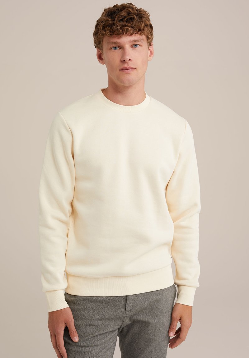 Light cream cotton sweatshirt with long sleeves, round neck, ribbed cuffs, and hem. The fabric is soft and textured, worn with gray pants.