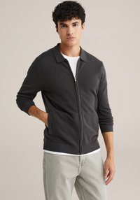 Temno sivi jopič z zadrgo, teksturiranim pletenjem, dolgimi rokavi in ravnim ovratnikom. Ima stranske žepe ter rebraste manšete in spodnji rob.