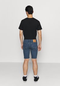 Mörk t-shirt, blå denimshorts som når mitt på låren, med bakfickor och en läderlapp. Svarta sneakers med vita sulor.
