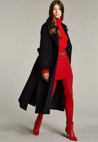 Cappotto lungo nero, dolcevita rosso a coste, mini gonna rossa, collant rossi e stivaletti rossi. Tessuti lisci con una cintura lucida come accentuazione.