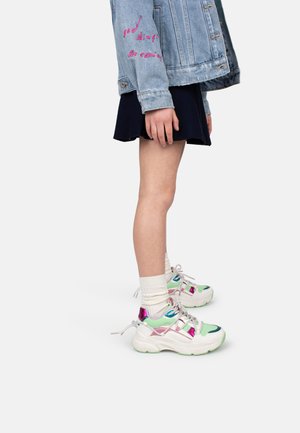 Baskets épaisses avec des accents blancs, vert menthe et irisés, dotées d'une semelle épaisse et de lacets, associées à des chaussettes blanches mi-mollet et une jupe marine.