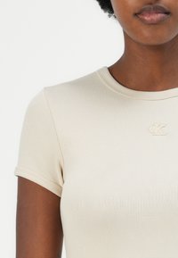 Beige fitted t-shirt with short sleeves and a ribbed texture. Features a small embroidered CK logo on the chest.