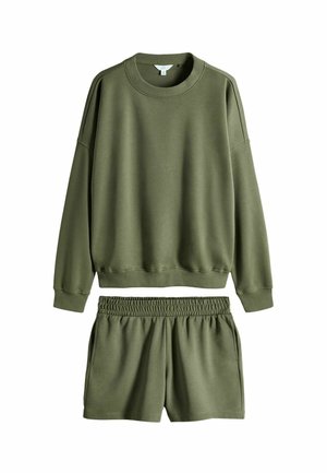 Olīvu zaļš džemperis ar apaļu kakla izgriezumu un nomestu plecu līniju, apģērbs ar atbilstošām brīvā piegriezuma šortiem, kuru jostasvieta ir elastīga un ir kabatas.