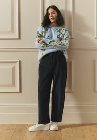 Svetlomodrý sveter s kvetinovým vzorom, čierne nohavice s voľným strihom a biele tenisky. Mäkká textúra, okrúhly výstrih a ležérny dizajn.