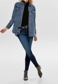 Denimjas met twee borstzakken, knoopsluiting en een ontspannen pasvorm, gecombineerd met donkerblauwe skinny jeans en gestreepte enkellaarsjes.