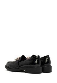 Schwarze Lackleder-Loafer mit niedrigem Blockabsatz, die vorne mit einer runden Schnallenakzent und einer glatten, glänzenden Textur versehen sind.