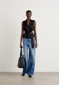 Black wrap top with a belt detail, paired with wide-leg light blue jeans. Holding a black leather bag. Smooth texture and modern silhouette.