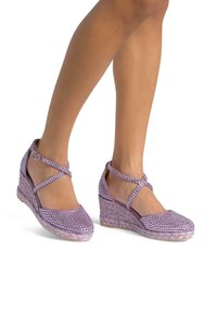 Scarpe a zeppa di lavanda con cinturini alla caviglia incrociati, decorate con piccole pietre luccicanti e suole in stile juta intrecciata. Texture liscia.
