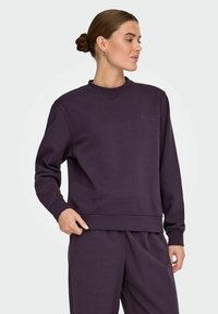 Lilla sweatshirt med rund halsudskæring og lange ærmer, lavet af blødt stof, med ribbede manchetter og et diskret logo på brystet.