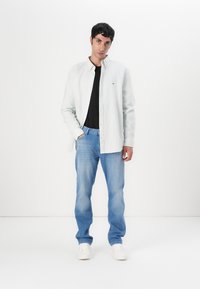 Chemise à rayures vert clair à manches longues, t-shirt noir en dessous, associée à un jean bleu clair et des baskets blanches. Design simple et coupe décontractée.