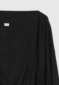 Camicia nera oversize realizzata in tessuto morbido, con un ampio scollo e spalle scese. L'etichetta riporta "zero waste."