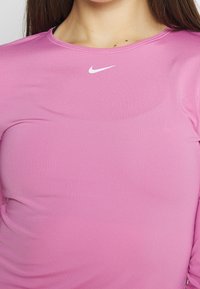 Růžové atletické tričko s dlouhými rukávy z texturované látky a bílým logem Nike na prsou. Kulatý výstřih s minimem švů.