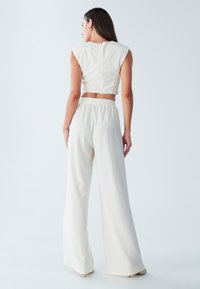 Bílý žebrovaný dvoudílný outfit skládající se z cropped topu s krátkými rukávy a vysokým pasem širokých kalhot, navržený s texturovaným povrchem.