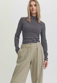 Gestreepte langwerpige top in navy en crème, gecombineerd met lichtbeige hoge geplooide broeken met een knoopsluiting en zijzakken.