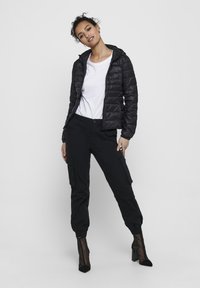 Black puffer jacket with a hood, featuring a quilted design. Paired with black cargo pants and sheer ankle boots. Simple white t-shirt underneath.