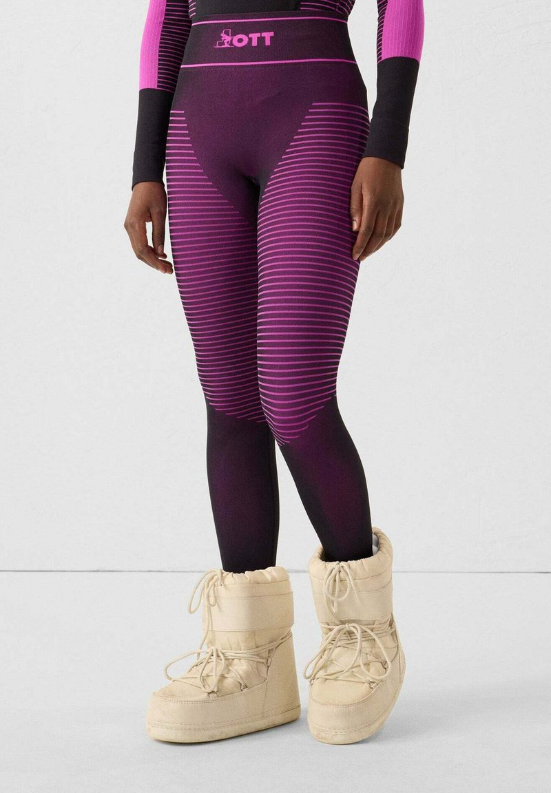 Leggings aderenti viola con righe orizzontali e una fascia alta in vita con il marchio rosa, abbinati a stivali morbidi color avorio fino al ginocchio.