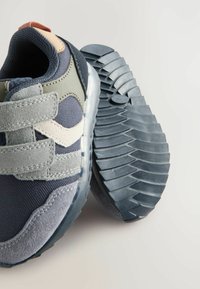 Sneakeren har en mørk marineblå mesh-overdel med grå ruskindsdetaljer, dobbelte Velcro-stropper og en struktureret gummisål med dybe riller.