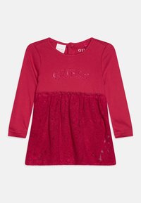 Vestido rojo de manga larga con parte superior de algodón y parte inferior de encaje. Logo "GUESS" en hilo brillante en el pecho. Etiqueta visible.