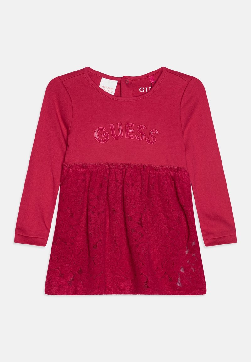 Vestido rojo de manga larga con parte superior de algodón y parte inferior de encaje. Logo "GUESS" en hilo brillante en el pecho. Etiqueta visible.