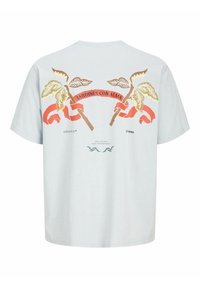 Lichtblauwe katoenen T-shirt met een grafisch ontwerp van gouden bladeren en een rode lint met de tekst "JARDINES CON ALMA" op de achterkant.