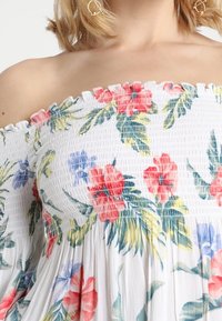 Šaty s odkrytými rameny vyrobené z bílé látky, s nařaseným živůtkem a květinovými vzory v červené, růžové, modré a zelené barvě. Hladká textura.