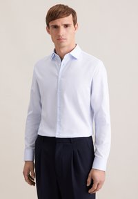Camicia azzurra a maniche lunghe con collo button-down, tessuto liscio e design aderente, abbinata a pantaloni scuri su misura.