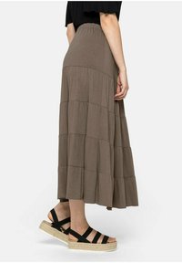 Falda maxi marrón de tejido ligero con cintura elástica, combinada con unas alpargatas negras con tiras sobre una superficie plana.