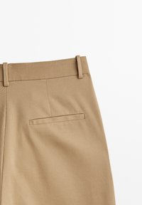 Beige skräddarsydda byxor gjorda av texturerat tyg, med en platt midja och en enda bakficka med en dold söm detalj.