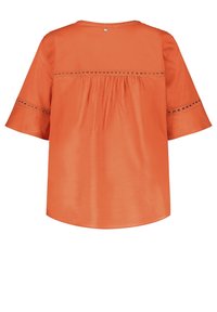Blusa arancione a maniche corte con scollatura tonda, caratterizzata da una schiena arricciata e cuciture decorative lungo le maniche. Tessuto con una superficie liscia.