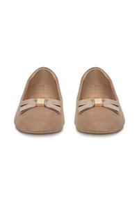 Mocasines de ante beige con suela plana, con un acento de lazo de tela y un detalle cuadrado en tono dorado. Diseño de punta redondeada. Textura suave.