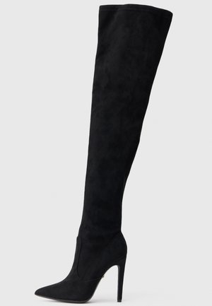 Juodos antkelių ilgio zomšinės botai su smailiu nosiniu ir aukštu stiletto kulnu. Lygus paviršius ir prigludusi forma sukuria elegantišką siluetą.