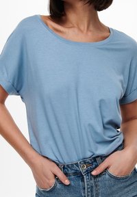 Light blue, short-sleeved t-shirt in a soft, lightweight fabric with a relaxed fit and scoop neckline, tucked into high-waisted denim jeans.