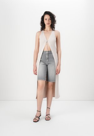 Light beige ribbed knitted long vest with a front tie, paired with gray denim shorts, and black strappy sandals. Smooth texture, open design.