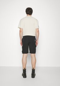 Beige bomulls t-skjorte, avslappet passform, korte ermer; parret med svarte cargo shorts med sidelommer, fullført med svarte ankelstøvler.