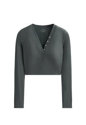 Korte langemouwtop in donkergroen. Gemaakt van ribbelstof met een V-hals en een knoopsluiting met vijf knopen. Soepele textuur, aansluitend ontwerp.