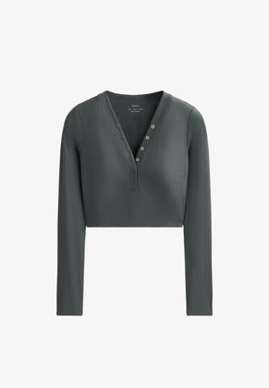 Korte langemouwtop in donkergroen. Gemaakt van ribbelstof met een V-hals en een knoopsluiting met vijf knopen. Soepele textuur, aansluitend ontwerp.