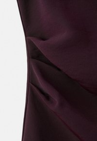 Tela de un púrpura oscuro con una textura suave, que presenta caídas sutiles y detalles plisados, exhibiendo un diseño moderno y una apariencia en capas.