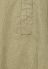 Tecido caqui com um padrão texturizado e tecido, apresentando um bolso lateral com detalhes de costura em contraste.
