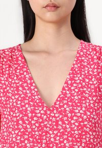 Rosafarbener Stoff mit floralem Muster, ausgestattet mit einem tiefen V-Ausschnitt und kurzen Ärmeln. Leichte, glatte Textur.