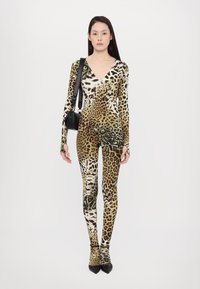 Bodist v vzorčku leoparda iz raztegljive tkanine z dolgimi rokavi in globokim V-izrezom. Usklajen z črnimi petami v koničasti obliki in majhno črno torbico.